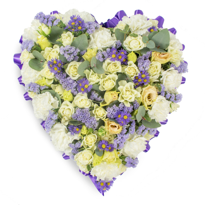 An elegant, closely packed heart-shaped floral tribute set against a plain white studio background, where the interplay of pale hues and rich accents creates a composed, consoling visual statement. The heart's outer edge is neatly framed with a continuous purple satin ribbon, its lustre and ordered loops supplying a dignified outline to the floral canvas. Within this border, clusters of cream and pale yellow roses dominate, ranging from tight, beadlike buds to petals gently parting-each bloom contributing to a soft, sumptuous surface of layered petals. Complementing the roses are full white carnations, their ruffled forms lending classical softness and a comforting weight. Delicate sprigs of lavender-hued statice ripple through the design, introducing small, paperlike textures and a cooling purple tone. Interspersed for contrast are small, vivid purple daisy-style blooms with prominent yellow centers; these provide lively punctuation against the gentler palette and draw the eye across the heart. Rounded eucalyptus leaves in blue-green tones are placed throughout to break up density, add sculptural shape, and imply a subtle herbal scent. The photographic lighting is soft and diffuse, emphasizing petal depth and the arrangement's hand-built structure. This composition reads as a mindful tribute-quiet, refined and suitable for funeral homes, chapels and graveside services around Harold Hill, Collier Row, and nearby neighbourhoods-conveying sympathy, steadfast love, and respectful remembrance in floral form.